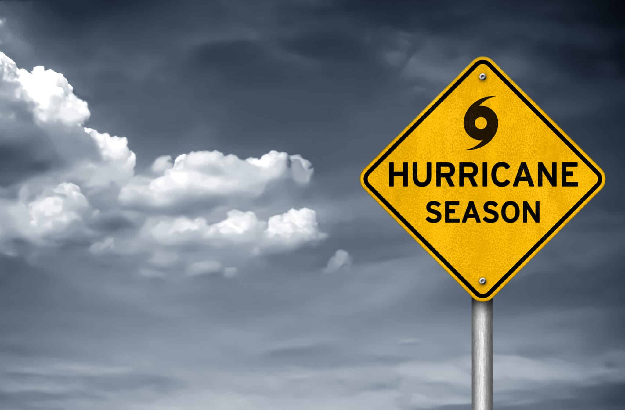 An image of a gray and stormy sky, with a yellow cautionary sign that reads “hurricane season”.